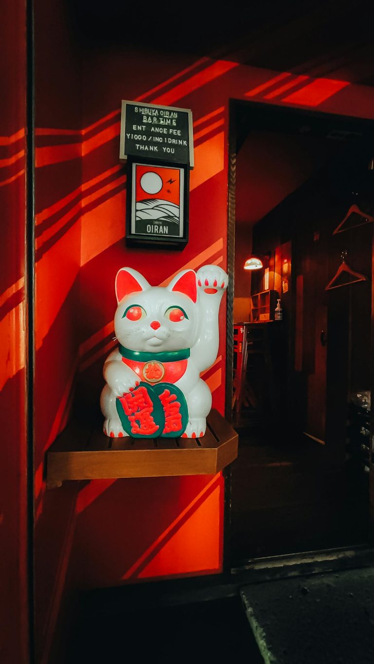 Maneki-neko statue in a brightly lit room with Japanese decor, Tokyo, Japan.
